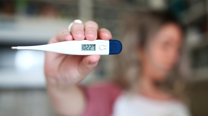 Person holding a digital thermometer showing a fever reading.