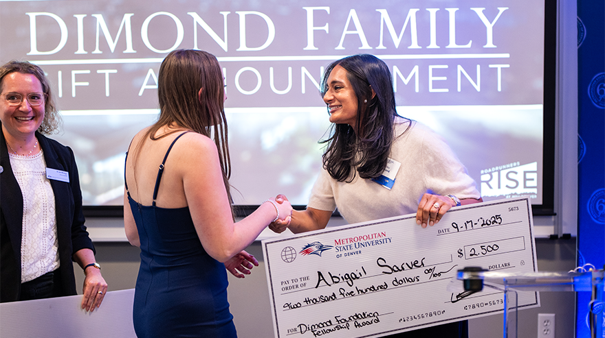 Two women shake hands during the Dimond Family gift announcement event while holding a ceremonial check.