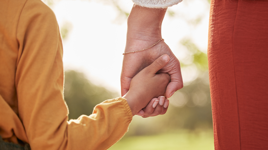Child holds an adult’s hand outdoors, representing Bring a Child to Work Day.