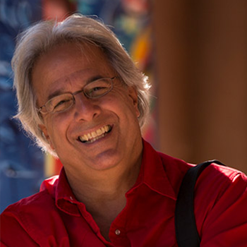 Headshot of Kenn Bisio smiling with a colorful window background.