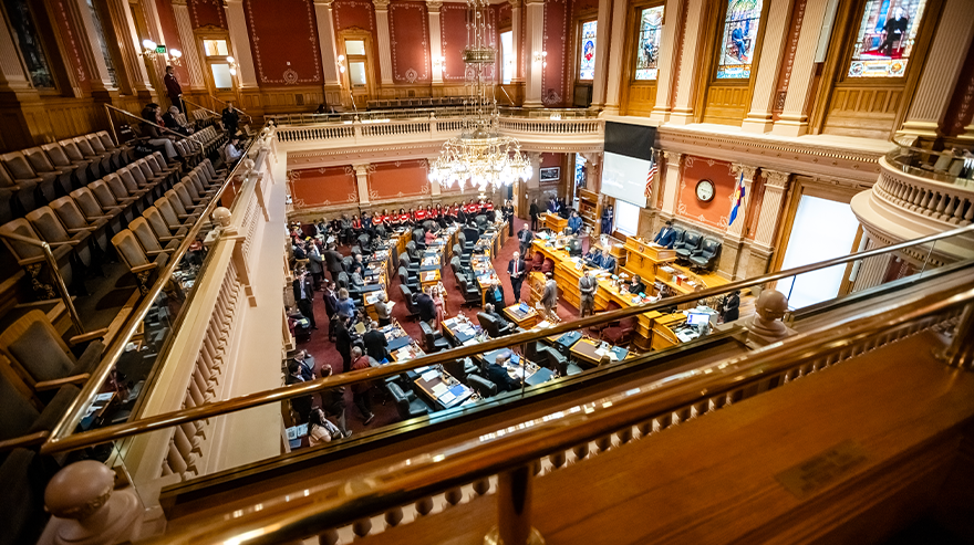 Students wearing red Roadrunners shirts stand in a line inside a government building, listening attentively during an event.