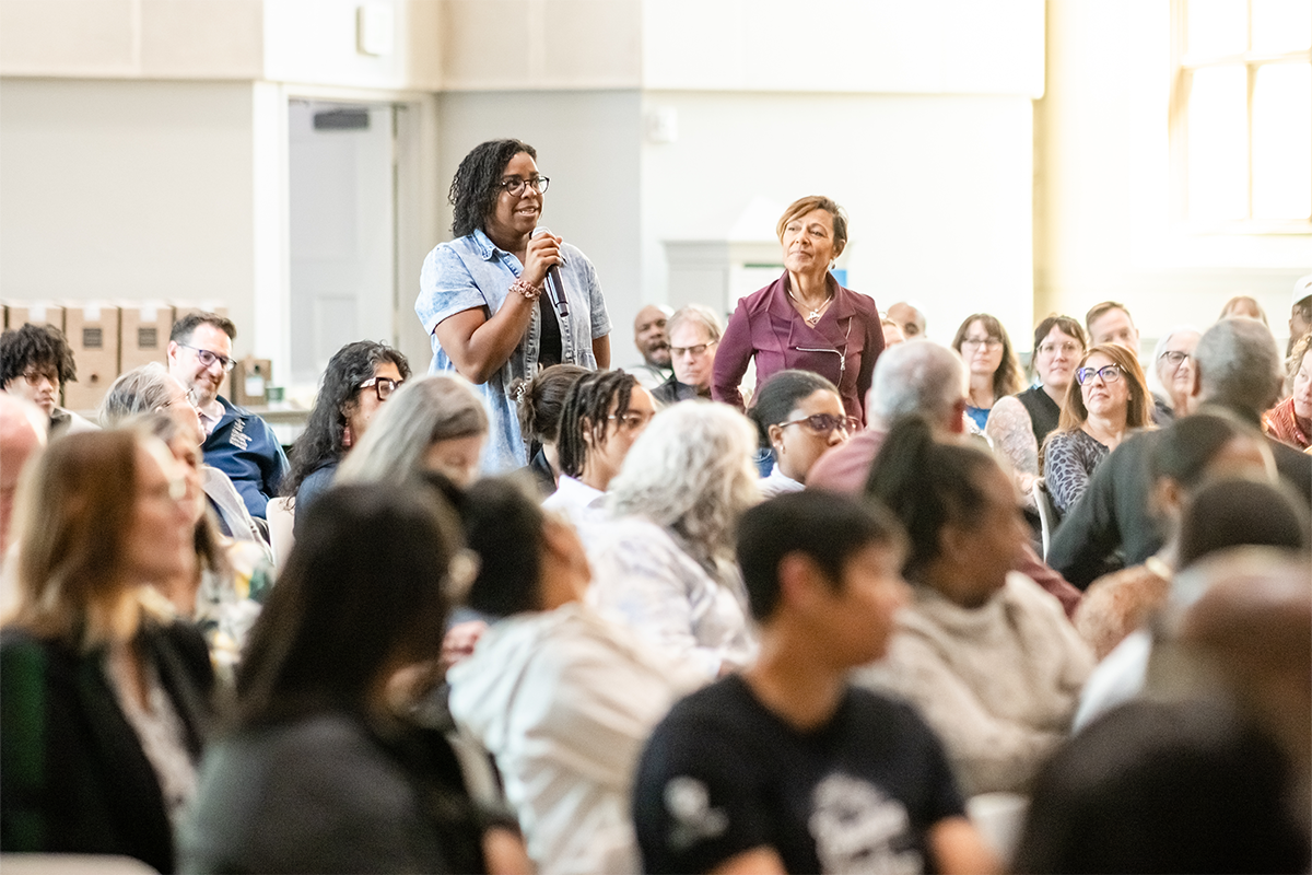 Audience member speaks into a microphone during an MSU Denver event while others listen in a crowded room.