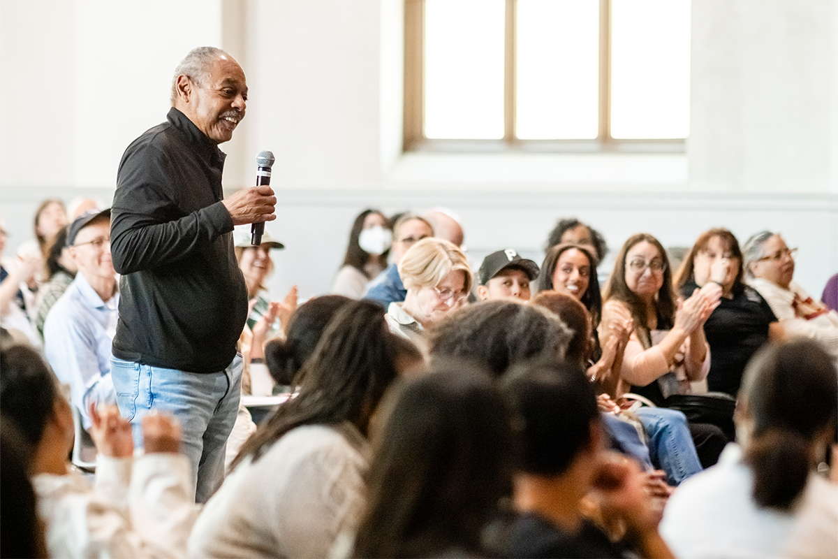 Audience member speaks into a microphone during an MSU Denver event while others listen in a crowded room.