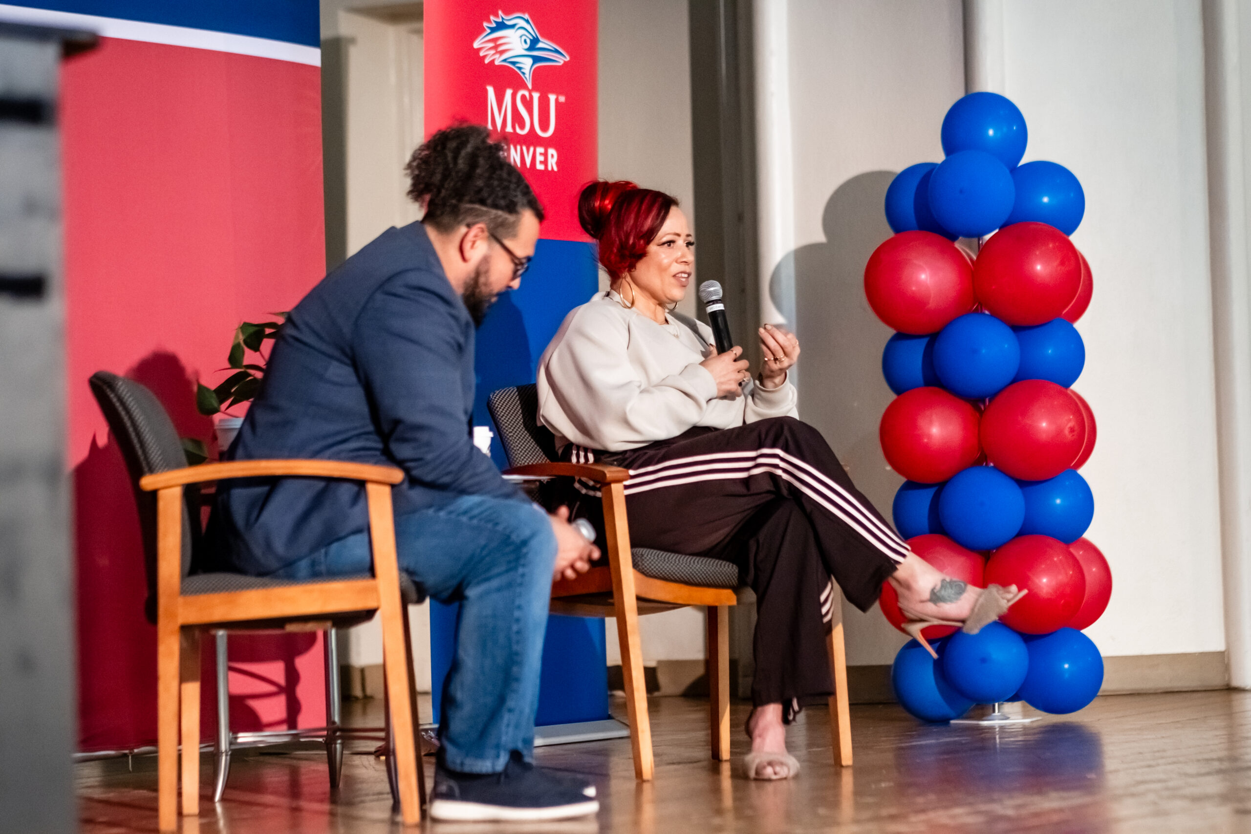 Woman speaks while a man watches on a stage with MSU Denver branding and colors.