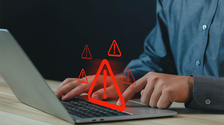 Person typing on a laptop with red warning icons overlaid on the screen, representing a security alert or potential cyber threat.