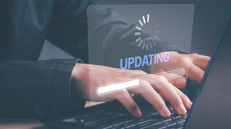 Close-up of hands typing on a laptop with a digital “updating” progress bar and loading icon overlay on the screen.