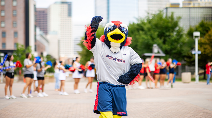 MSU Denver Roadrunner mascot Rowdy waves on campus with students and cheerleaders in the background.
