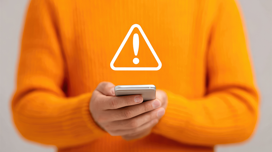 Person in an orange sweater holding a smartphone with a warning icon displayed above it, symbolizing a security or privacy alert.