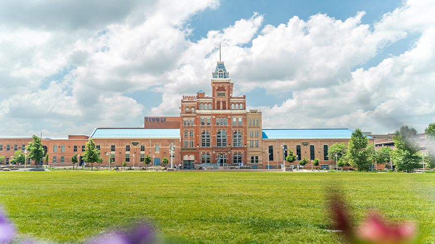 Wide view of the Tivoli building on the Auraria Campus with a grassy lawn in the foreground and clouds overhead.