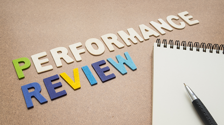 The words “Performance Review” spelled out in colorful letters next to a notepad and pen, representing annual employee evaluations.