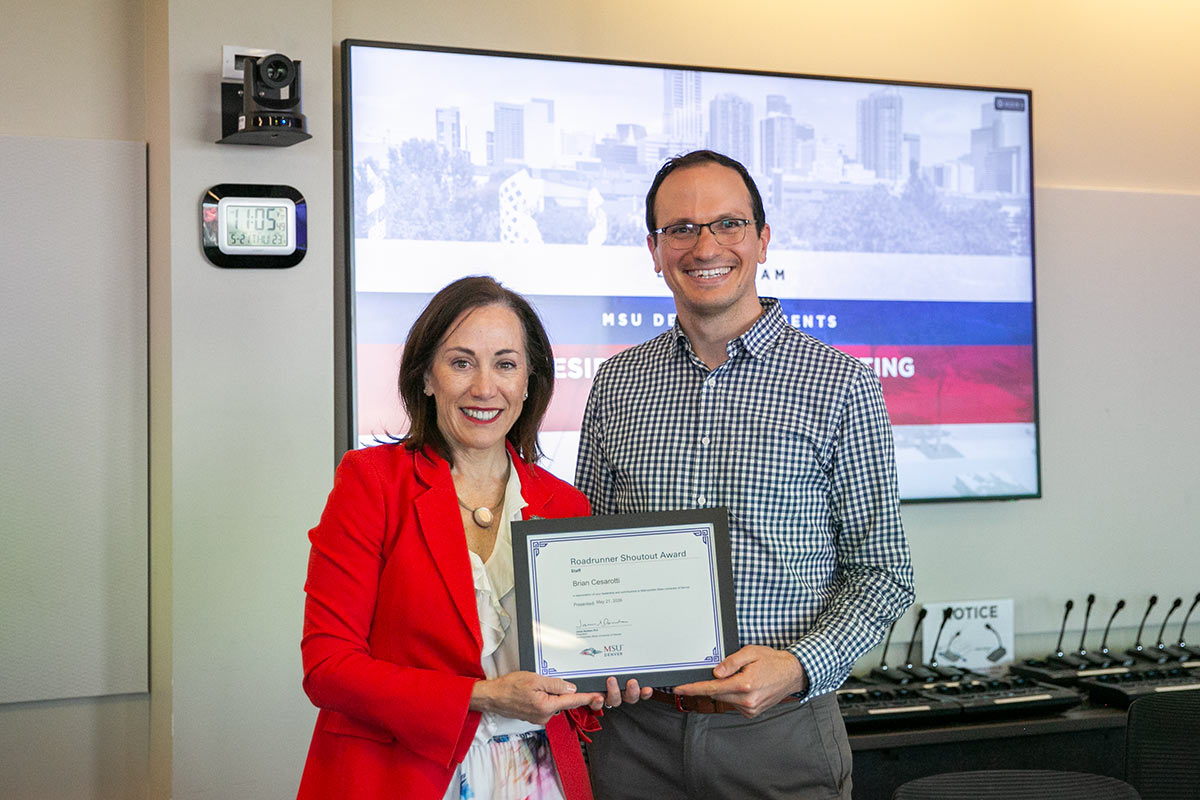 President Janine Davidson and Brian Cesaroti hold a framed award honoring Cesaroti at the President's Cabinet meeting.