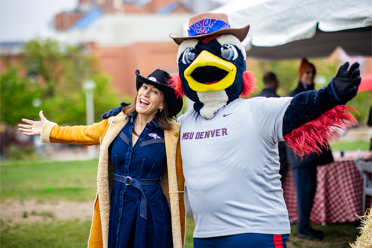 Woman in western attire posing with the MSU Denver Roadrunner mascot during a spring BBQ event outdoors.