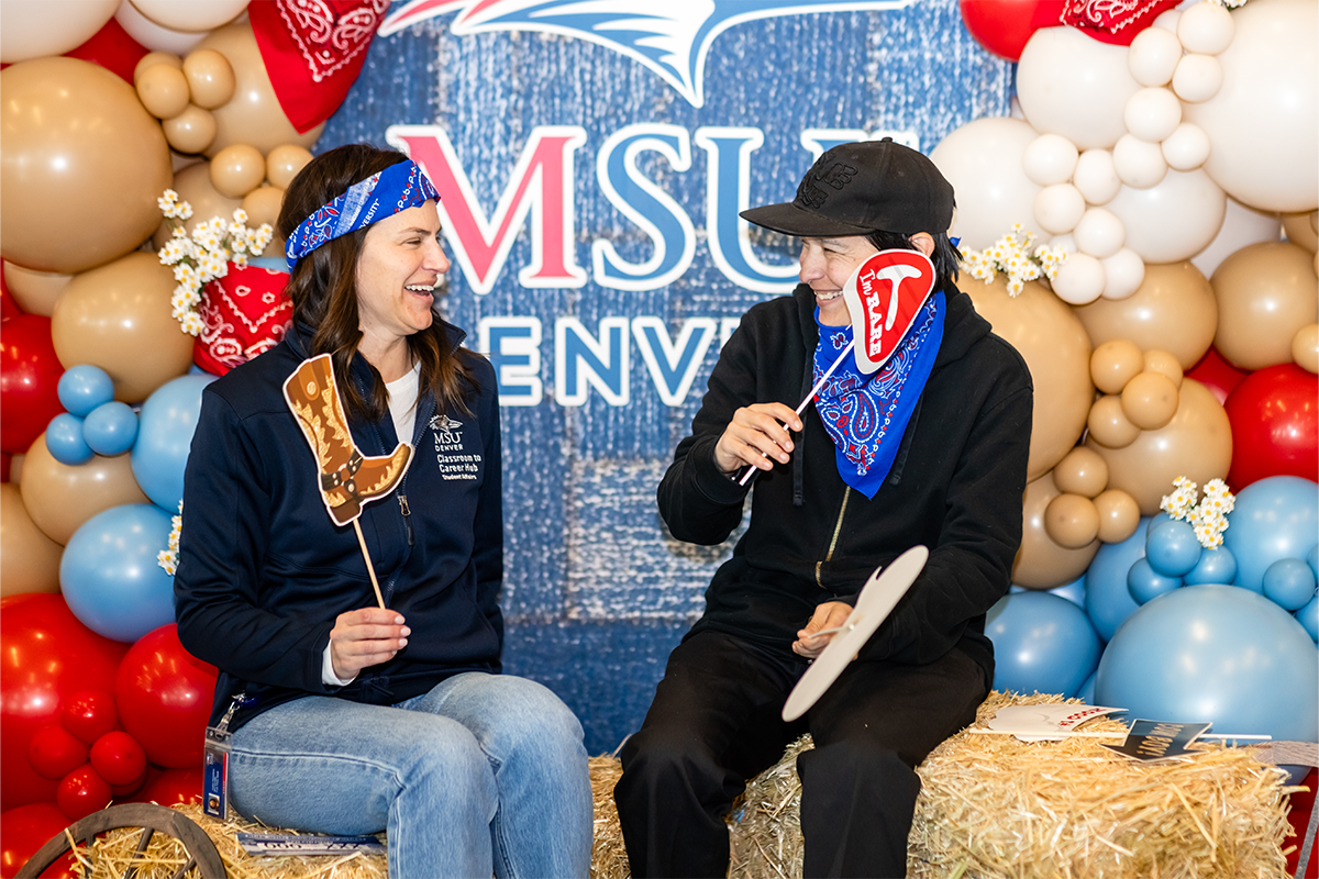 Two MSU Denver community members posing with western-themed photo props in front of a balloon backdrop during the Spring 2026 Howdy Rowdy BBQ event.