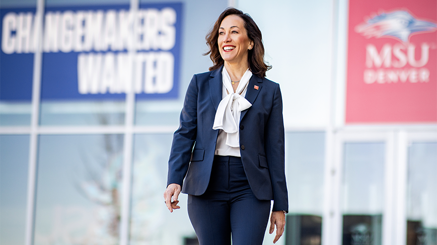 Janine Davidson is pictured walking in front of a building with banners displaying the MSU Denver logo and "Changemakers Wanted" slogan.