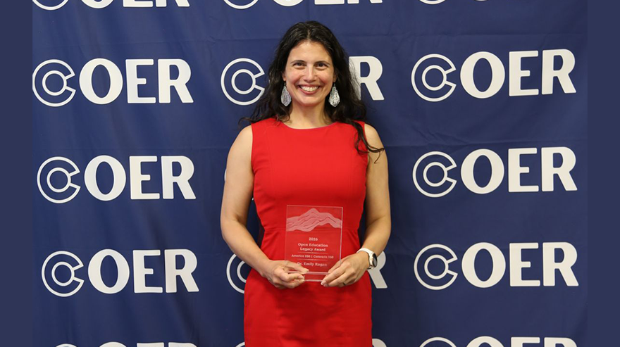 Emily Ragan stands holding a clear plaque while wearing a red dress and standing in front of a blue banner with the Colorado Open Educational Resources logo.