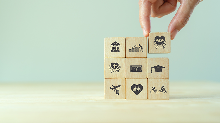 A hand is shown placing a wooden block among a stack of others that all show icons symbolizing employee benefits.
