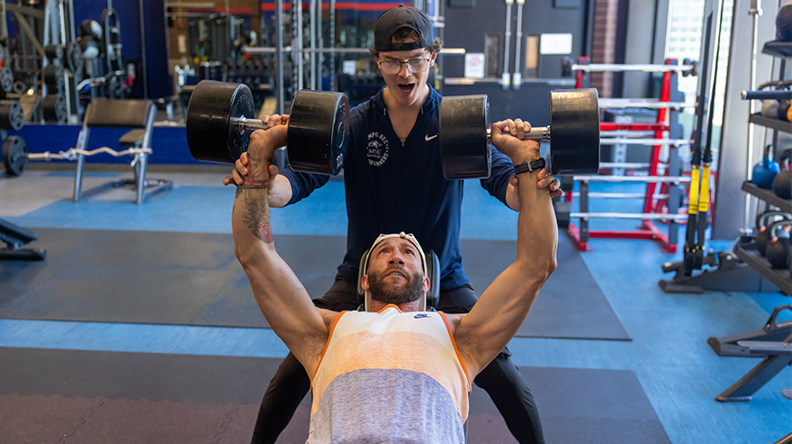 A trainer helps an exerciser complete an incline dumbbell press rep in the University gym.