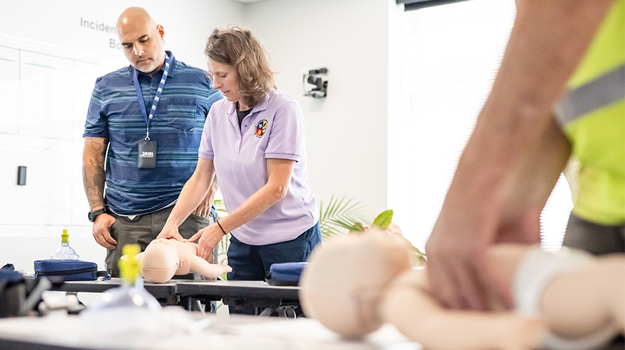 An instructor demonstrates techniques on a CPR baby mannequin next to a class attendee