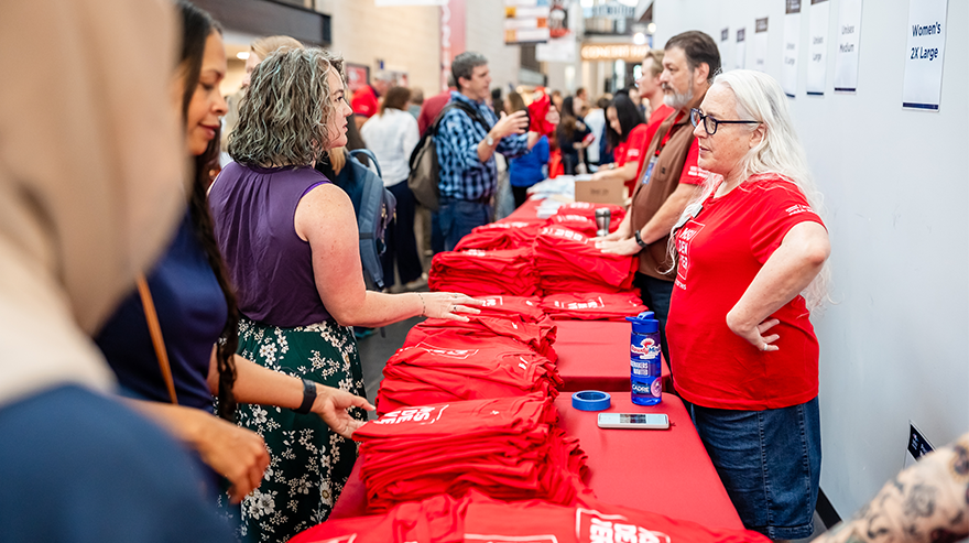 Employees browse red, MSU Denver-branded T-shirts on a table overseen by staff wearing the same shirt.