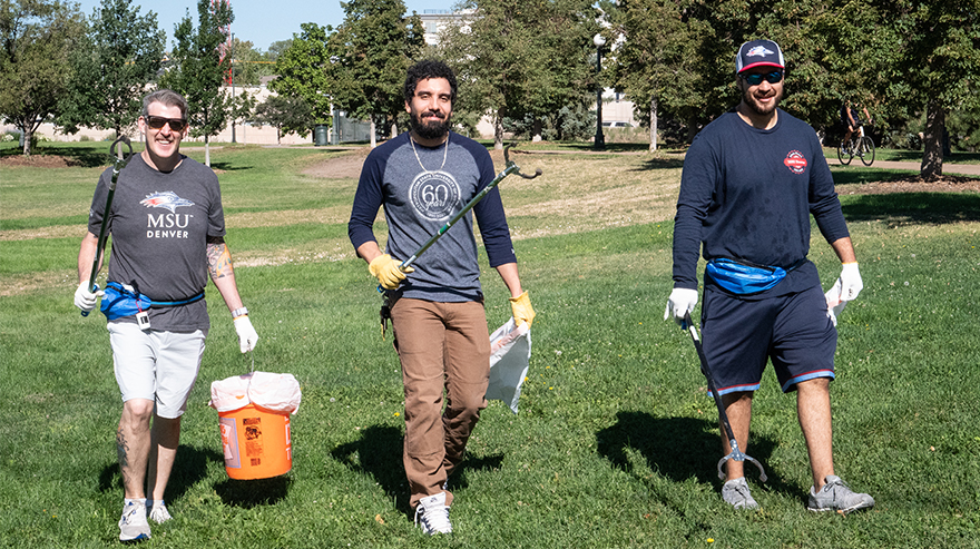 Three men holding equipment for picking up trash are pictured while walking in a park