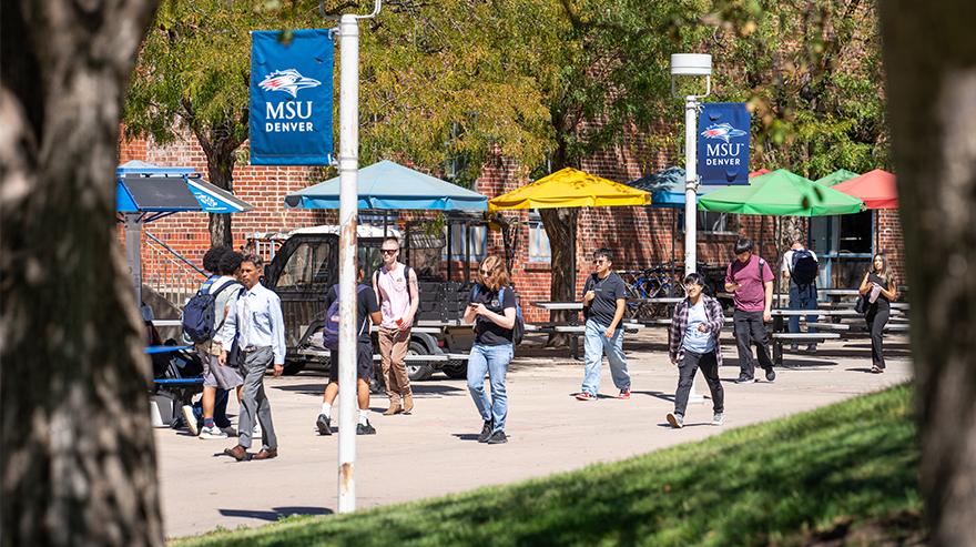 People walk on a campus sidewalk under MSU Denver banners